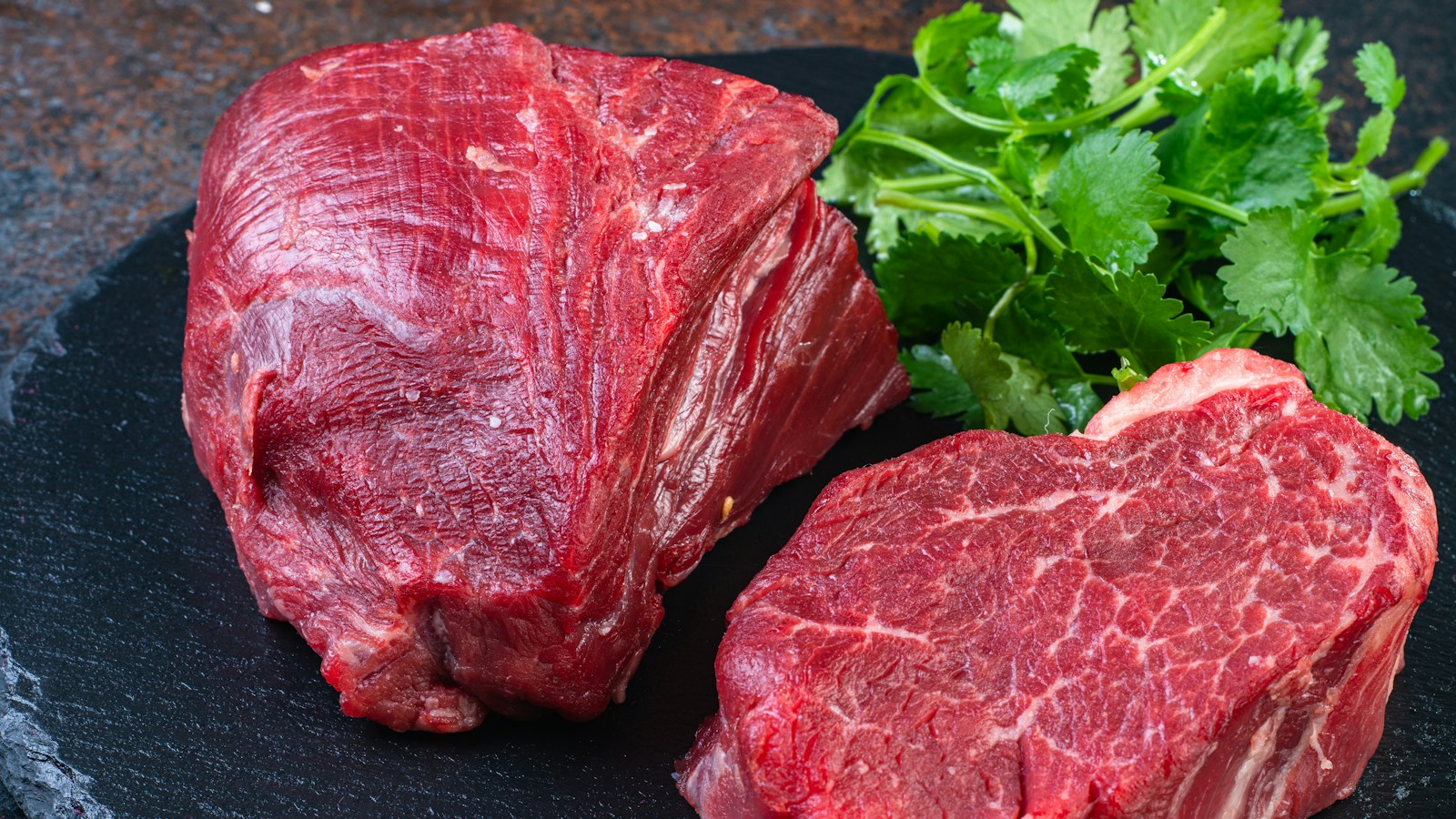 Two cooked steaks on a plate with parsley; the meat type is unspecified