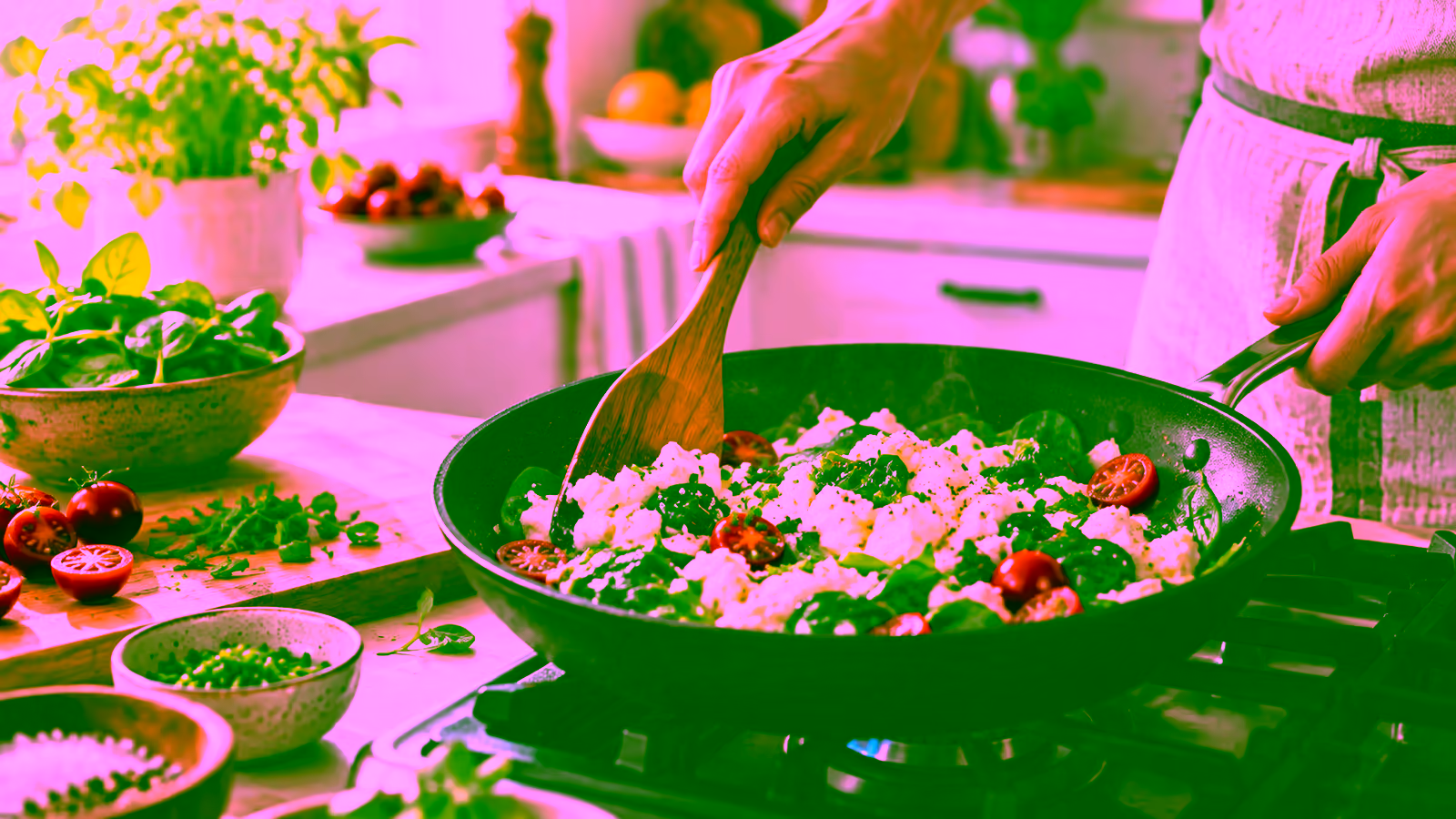 Egg whites cooking gently in a skillet with spinach, herbs, and tomatoes