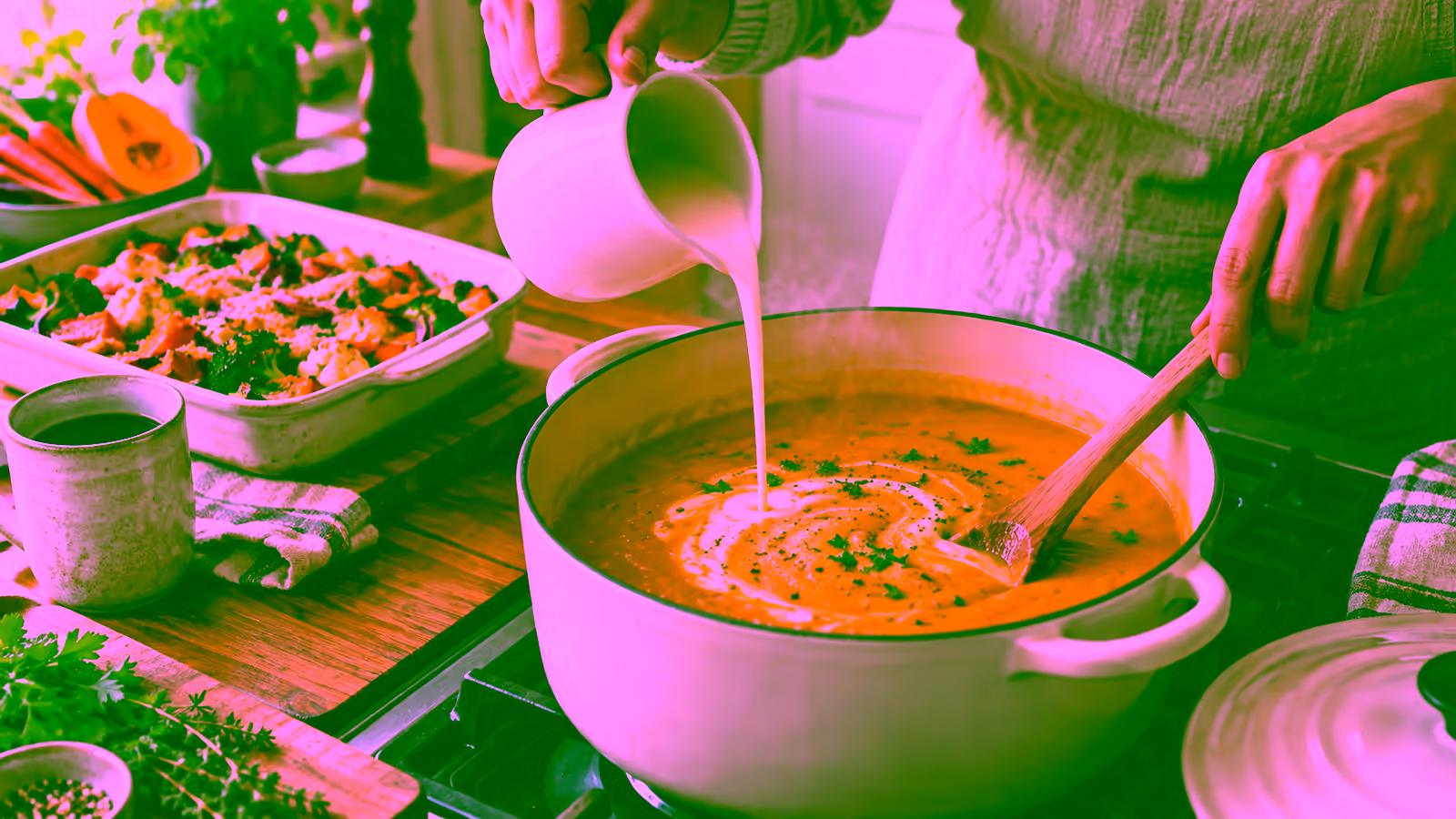 Evaporated milk being stirred into a creamy vegetable soup beside a baked casserole and coffee