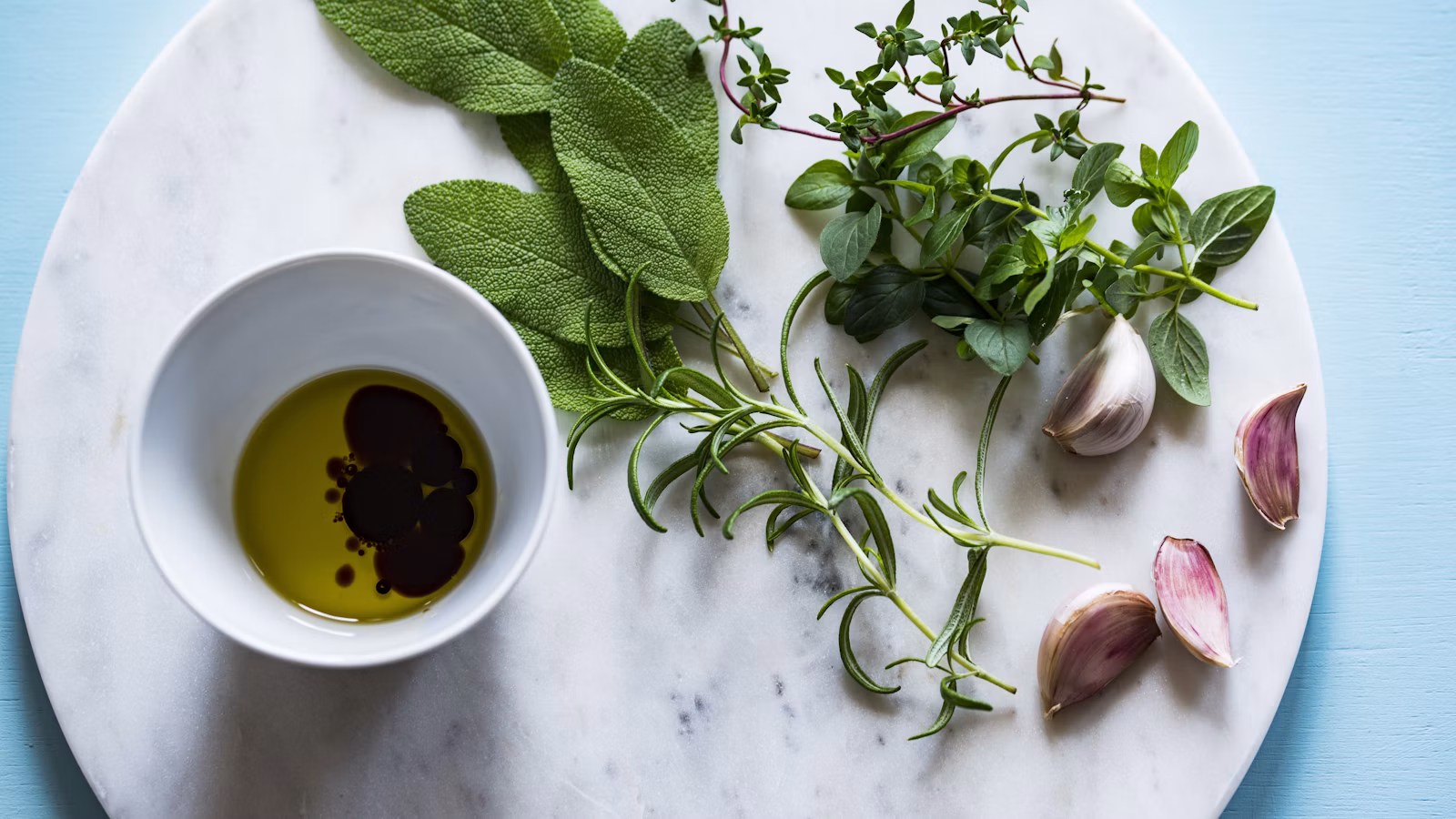 Garlic, olive oil, herbs, and bread on a kitchen table