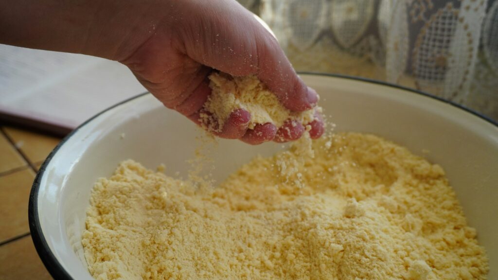 Hand scattering coarse yellow flour into a mixing bowl