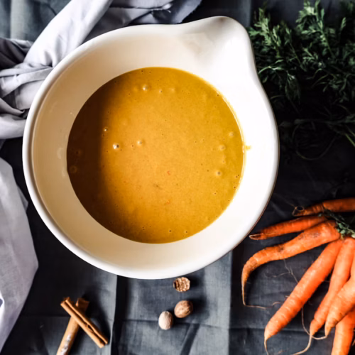 Golden broth in a bowl beside carrots and garlic