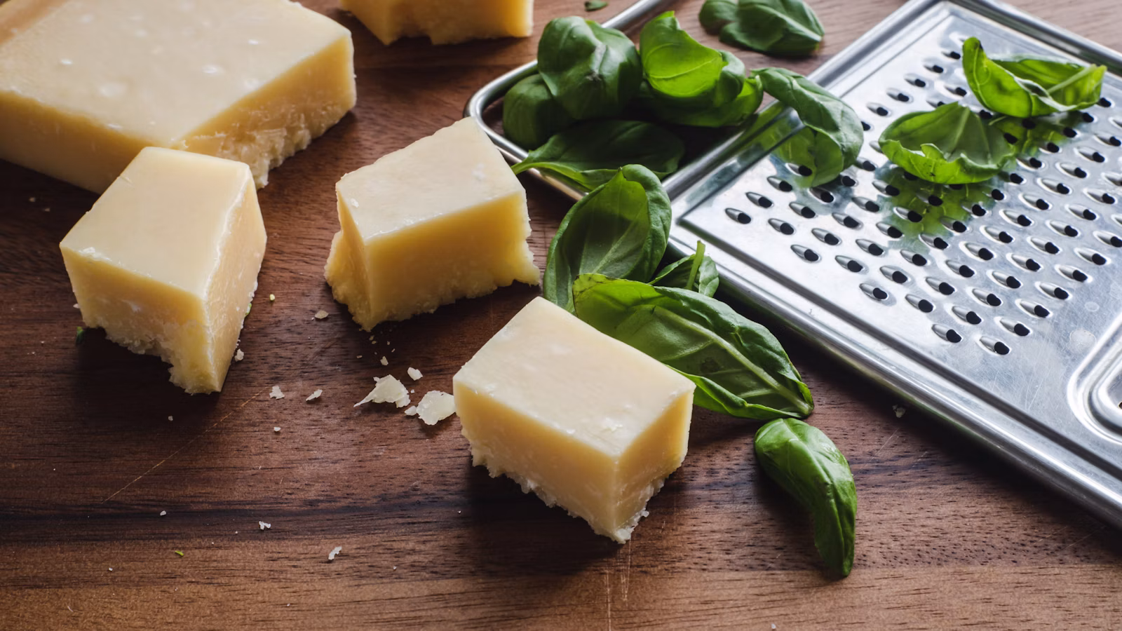 Sliced firm cheese beside green leaves on a wooden table