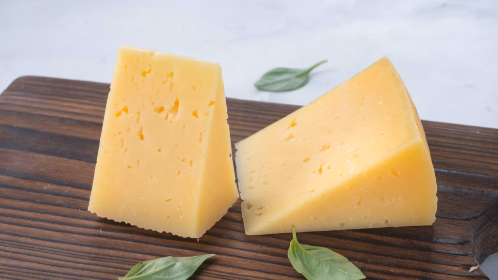Wedges of firm cheese on a wooden cutting board