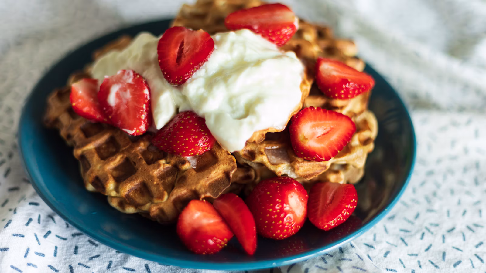 Waffles with strawberries and a creamy topping on a blue plate