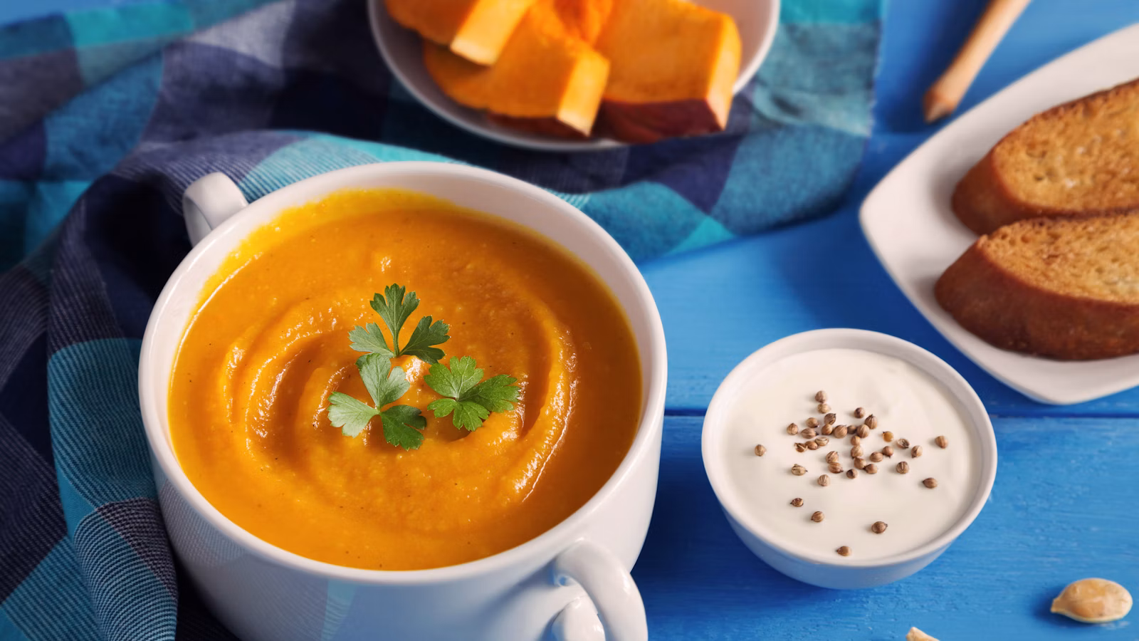 Smooth orange pumpkin coconut soup served with green herbs in a white bowl