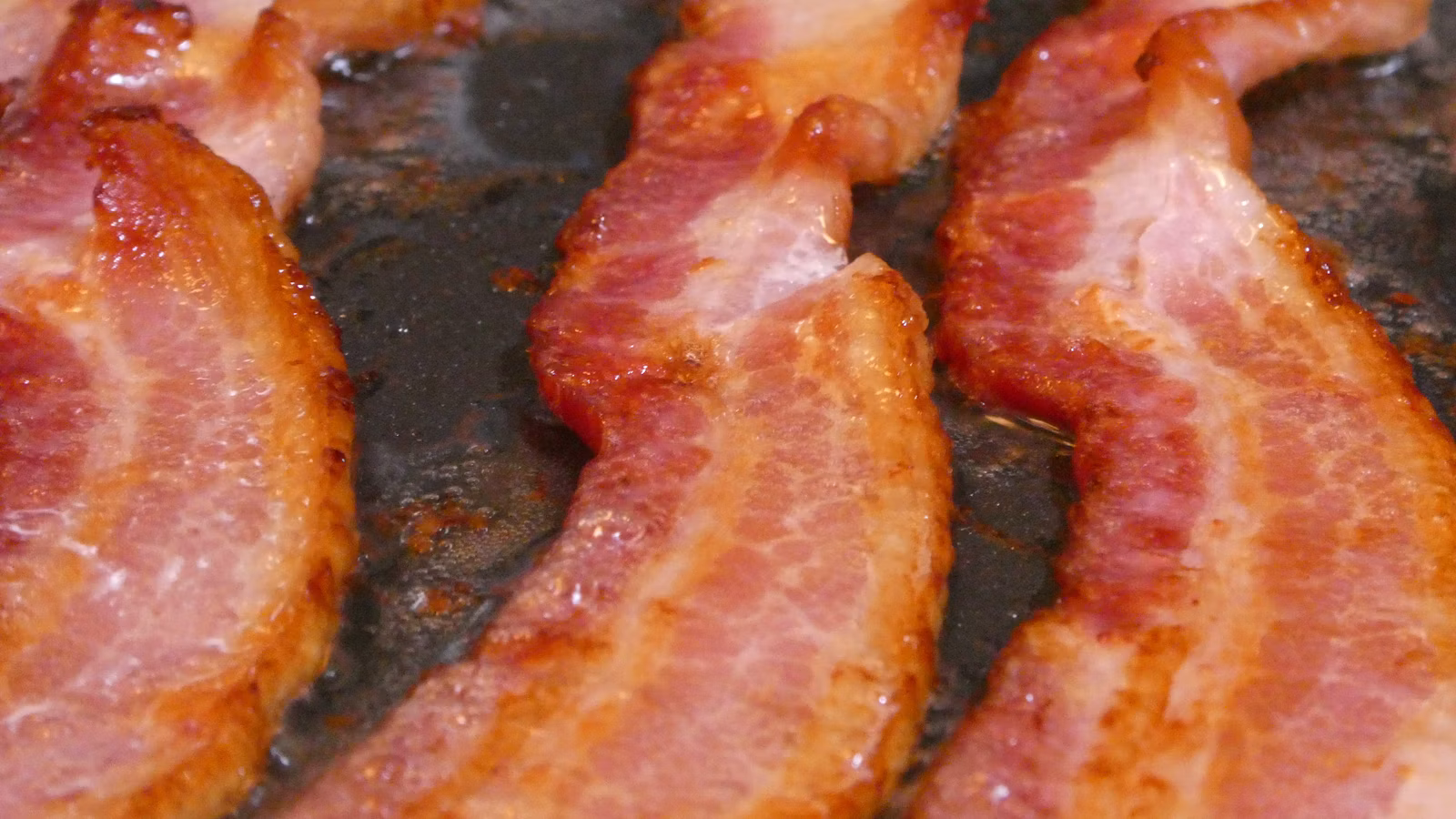 Bacon thick cut into wide strips cooking in a frying pan