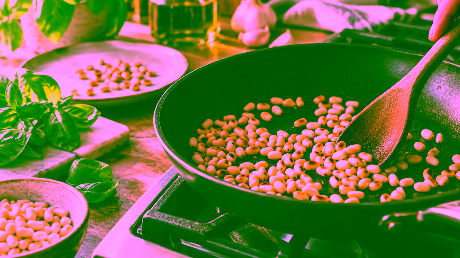 Pine nuts toasting lightly in a small skillet beside a wooden spoon