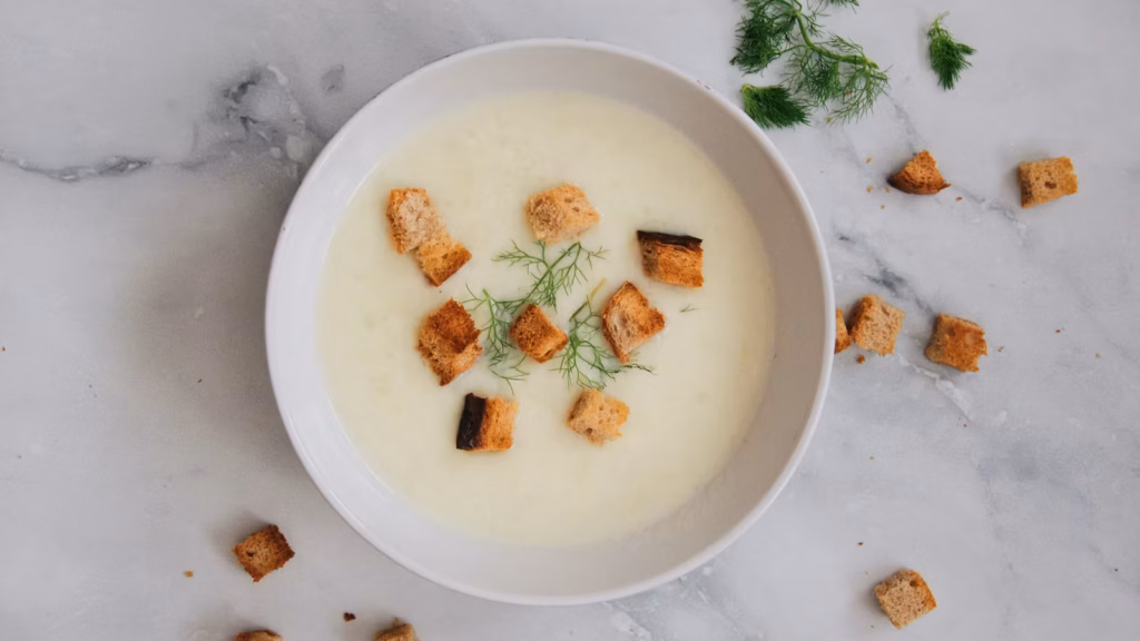 Smooth pale soup in a white bowl with a green herb garnish