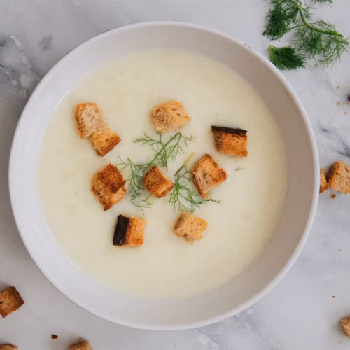 Smooth pale soup in a white bowl with a green herb garnish