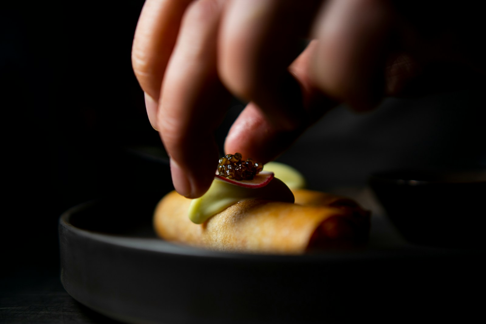 A hand adding a small spoonful of caviar to a prepared bite