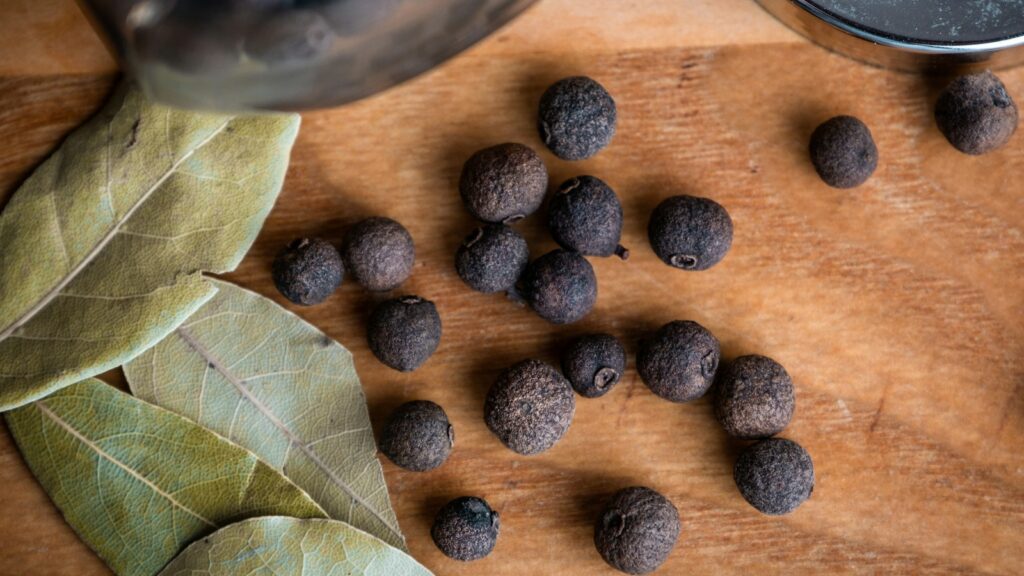 Whole allspice berries beside bay leaves on a wooden board