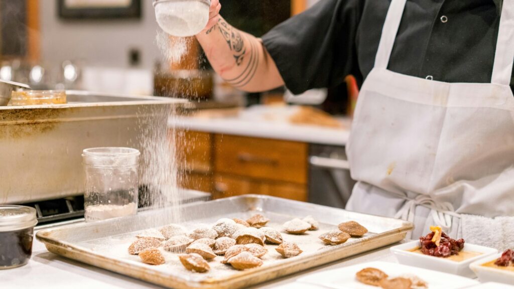A cook sprinkling flour over dough at a kitchen counter