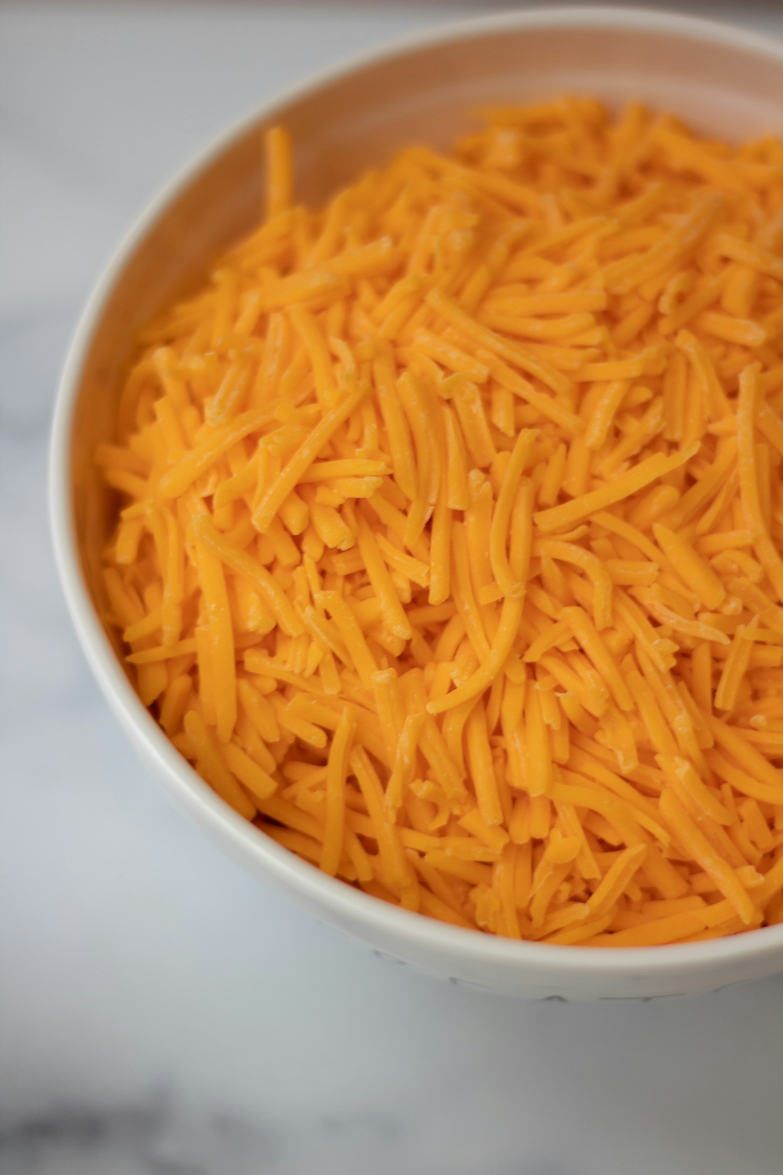 Shredded cheddar cheese in a white bowl