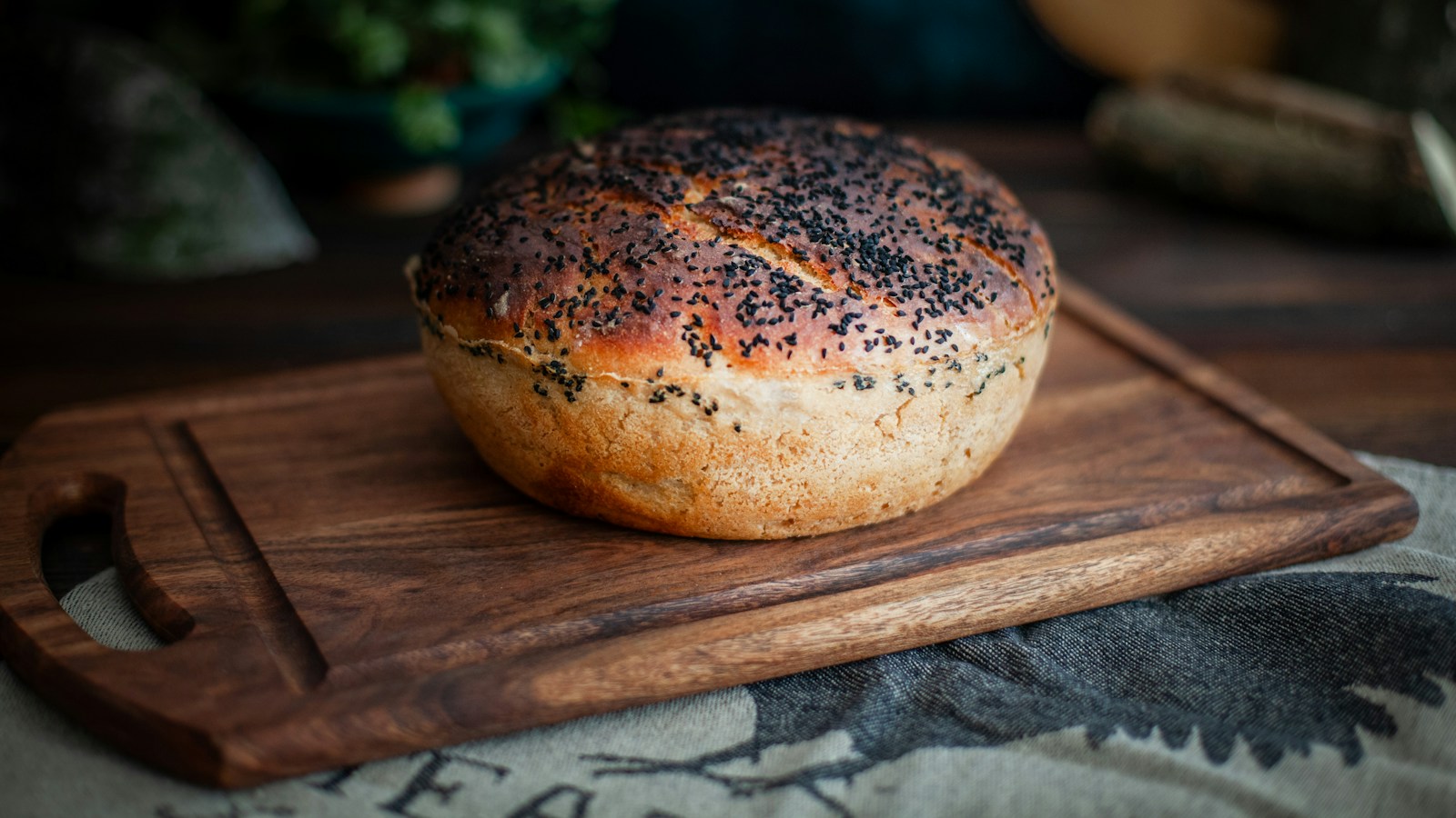 A round loaf topped with black sesame seeds on a wooden board