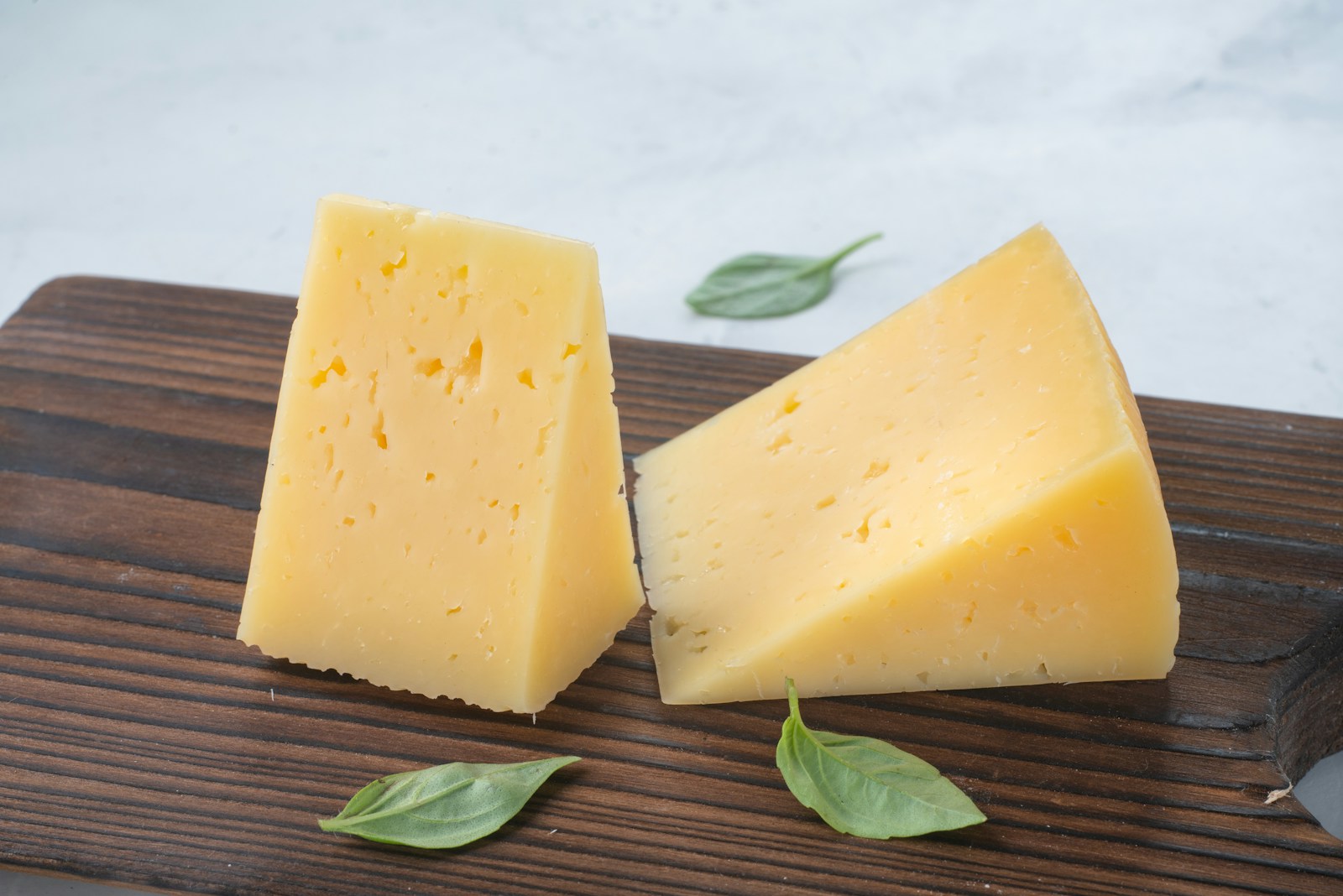 Two wedges of yellow cheese on a wooden board