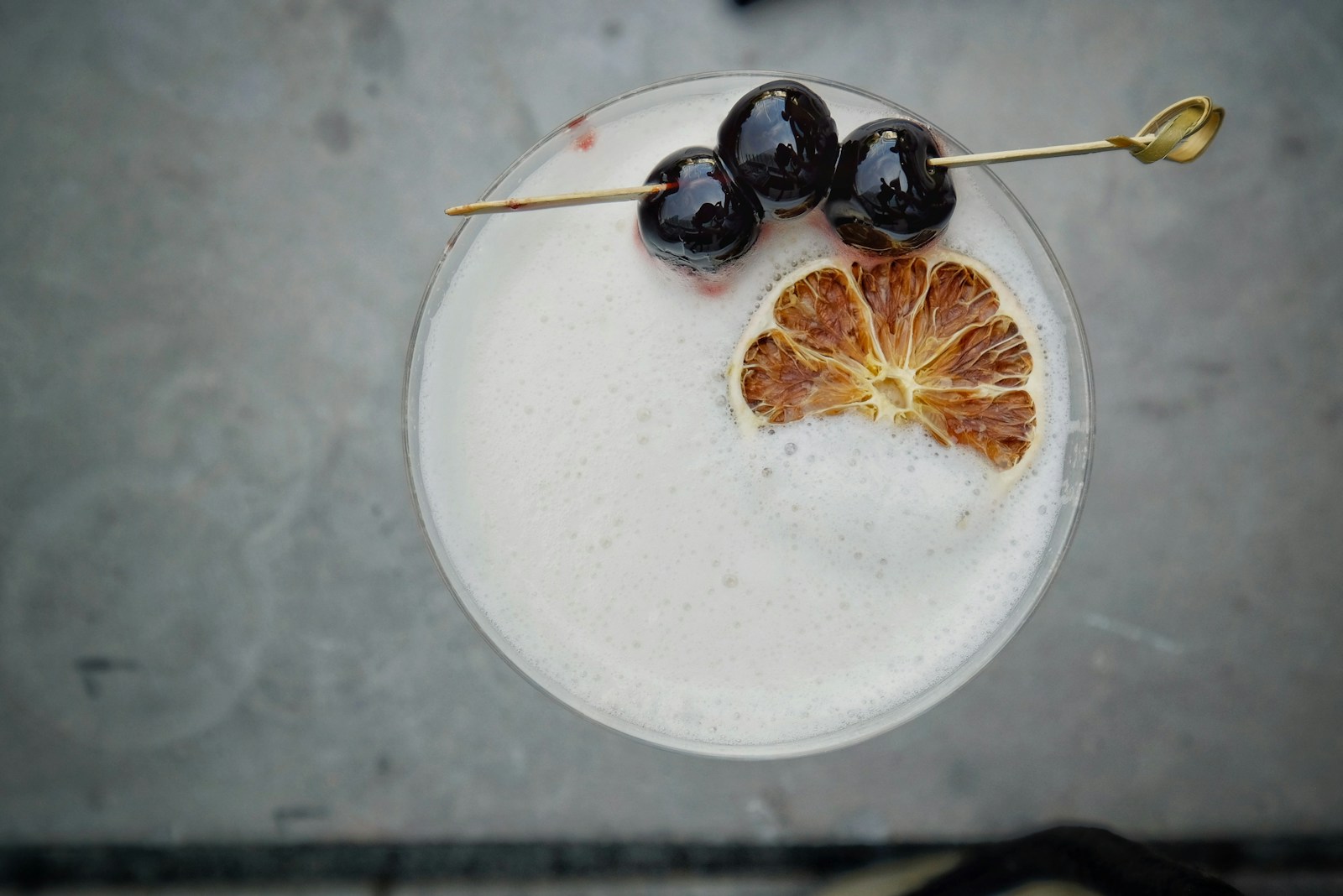 A drink topped with dark cocktail cherries on a pick