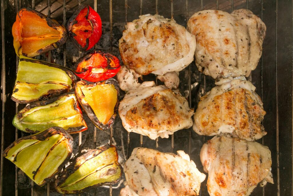 Grilled chicken thigh pieces and vegetables on a barbecue