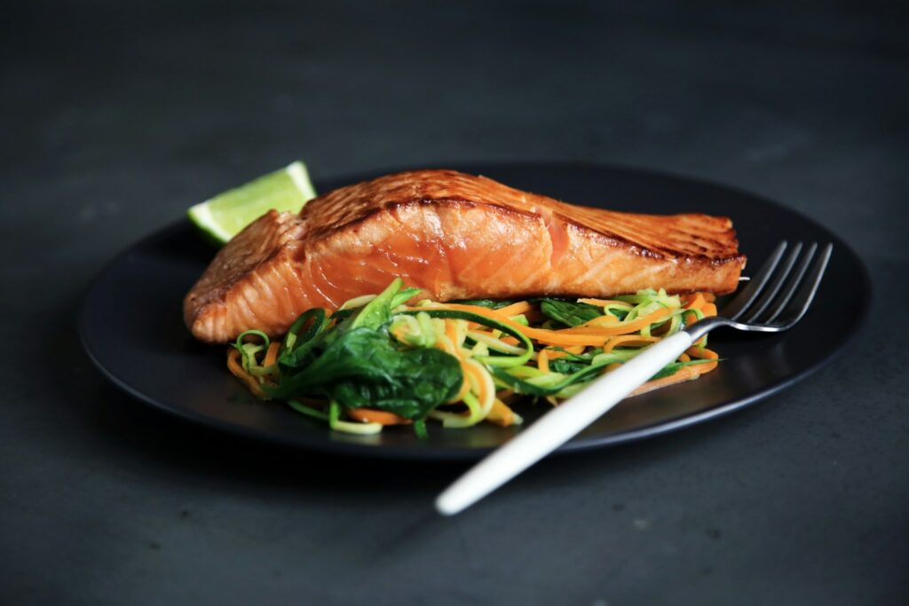 A cooked salmon fillet with vegetables on a black plate