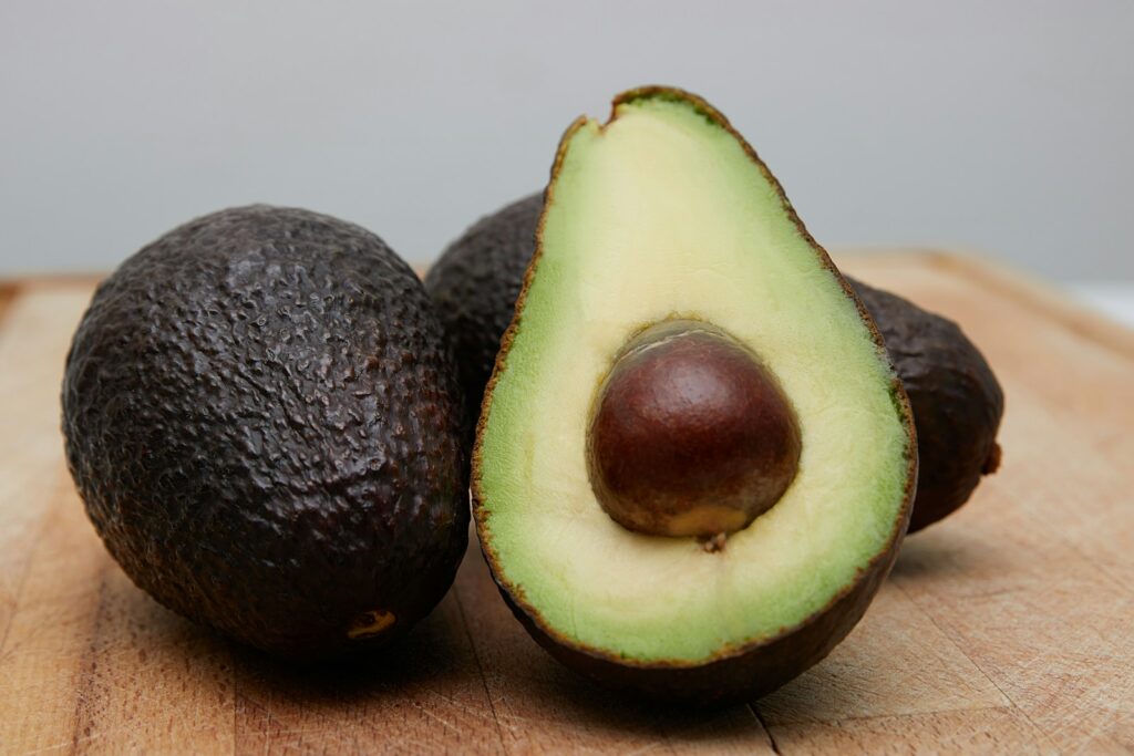 A cut avocado beside whole avocados on a wooden surface