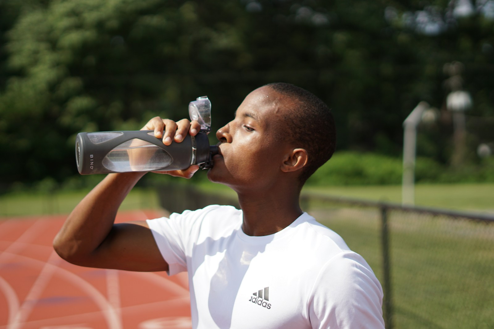 Person drinking water beside a running track