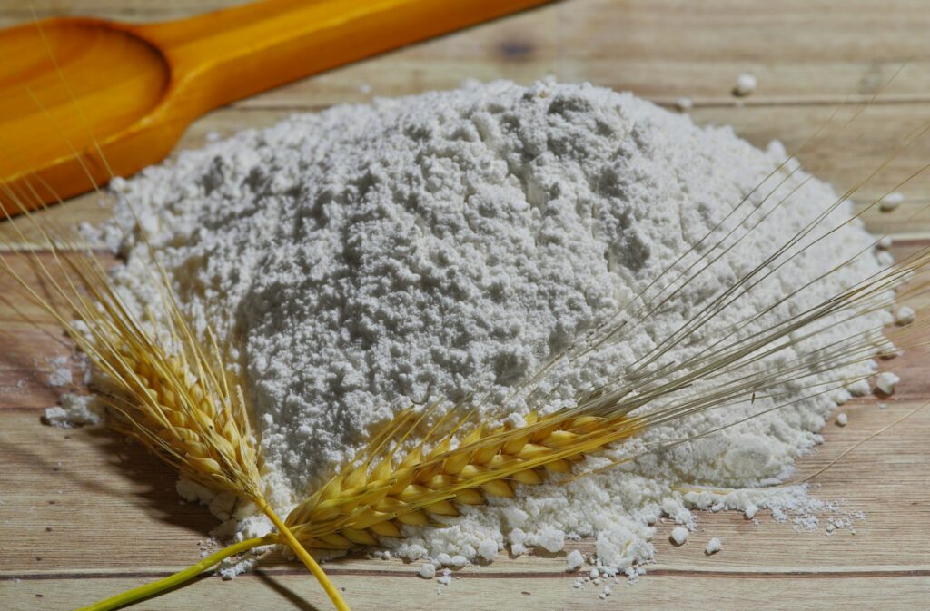Flour, wheat stalks, and a rolling pin on a wooden surface