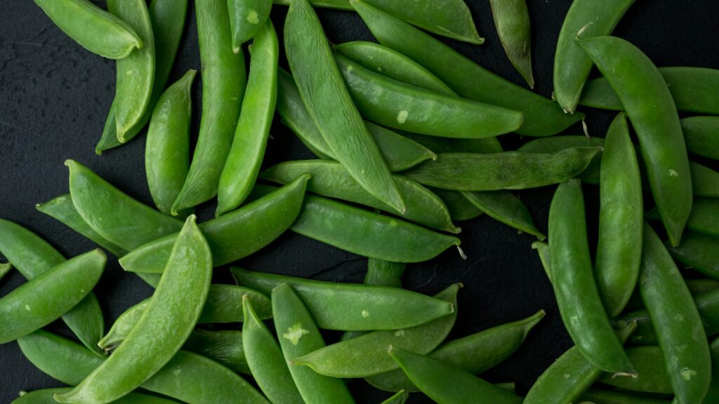 Fresh flat snow pea pods on a dark surface