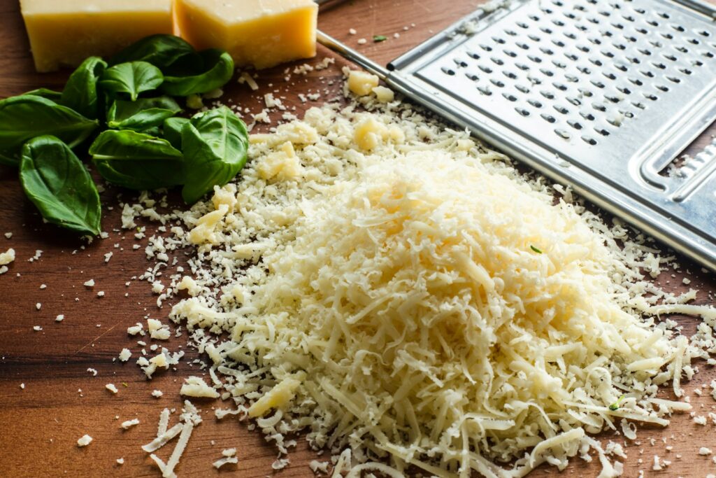 Freshly grated cheese beside a metal grater and cheese blocks