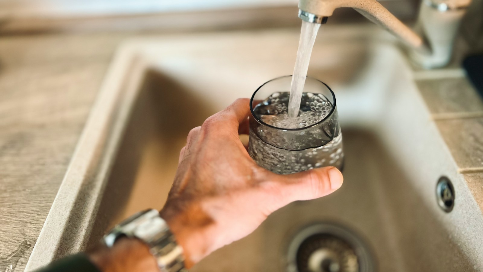 A hand holding a glass under a running tap
