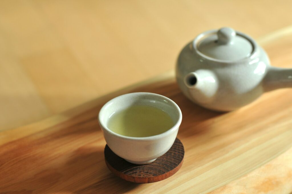 A cup of green tea beside a ceramic teapot