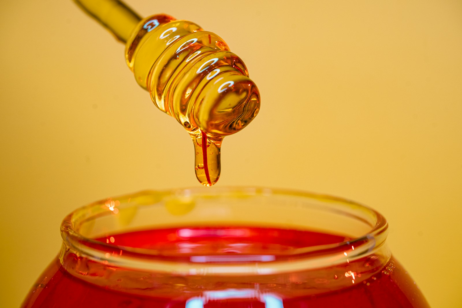 Golden honey dripping from a dipper above a jar