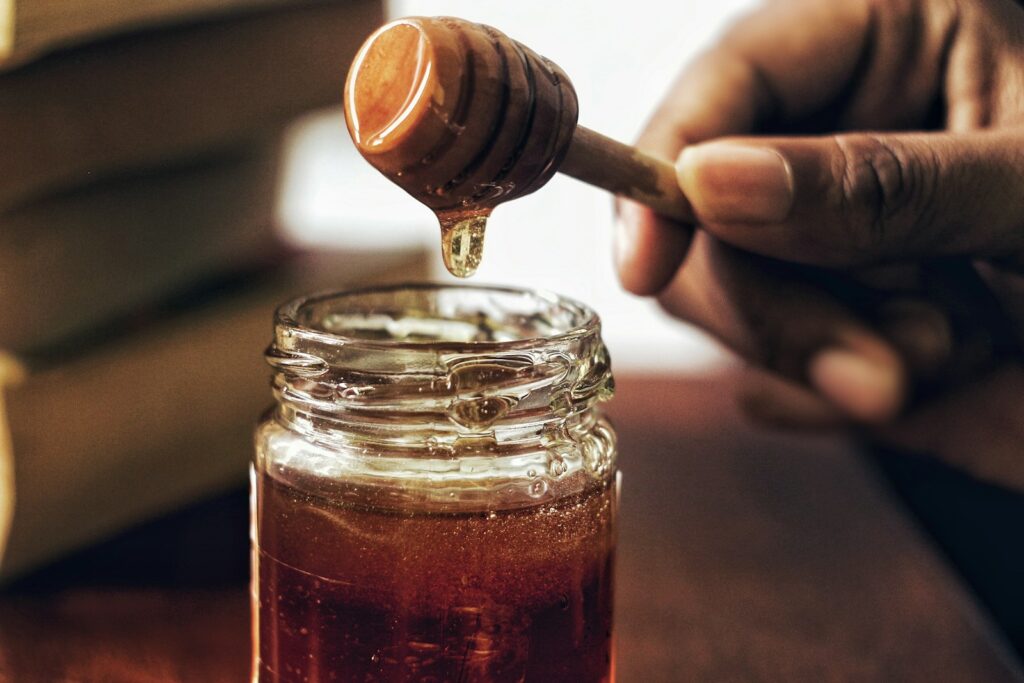 Honey dripping from a wooden dipper into a glass jar