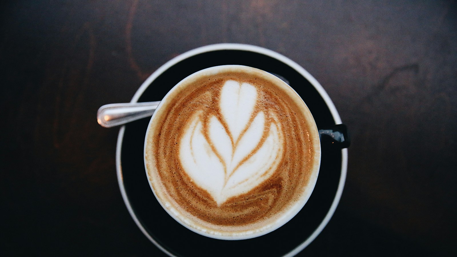 A cup of coffee with leaf-shaped latte art and a spoon