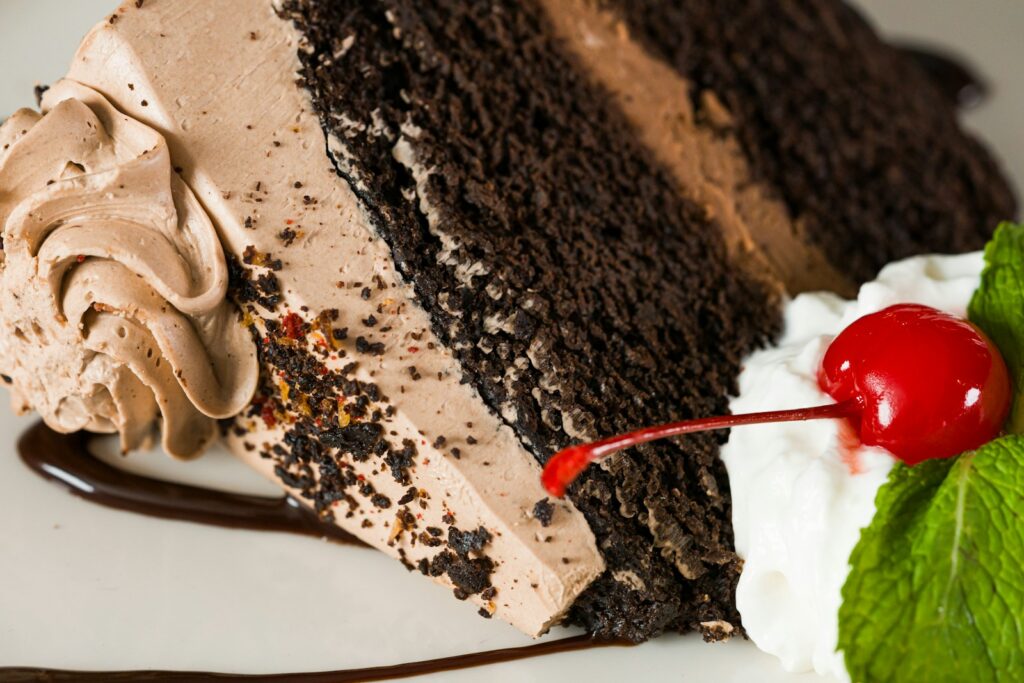 Chocolate cake slice with cream and a bright red cherry