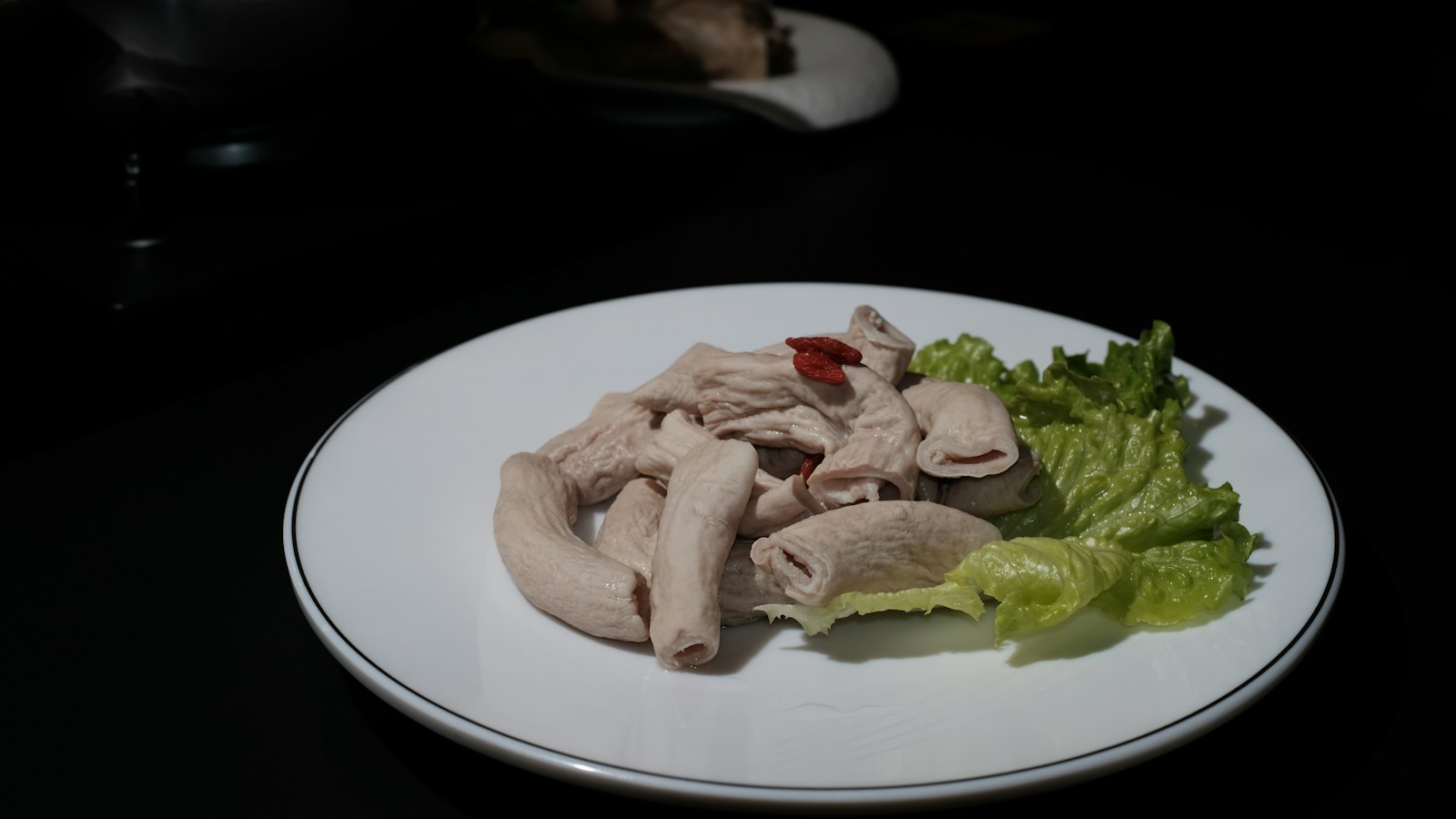 Pale beef tripe pieces on a white plate with lettuce
