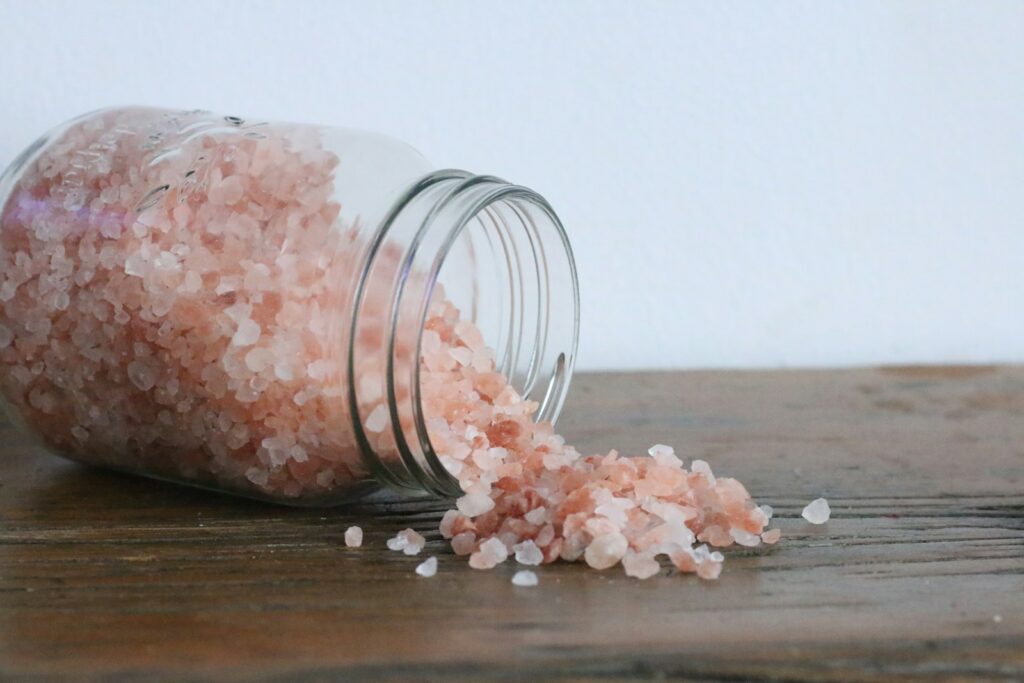 Pink salt crystals spilling from a glass jar onto wood