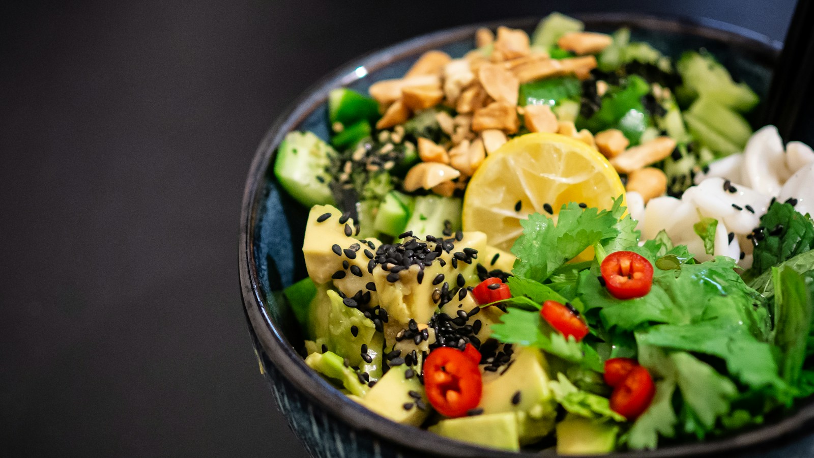 A rice bowl with avocado, cucumber, herbs, and black sesame seeds