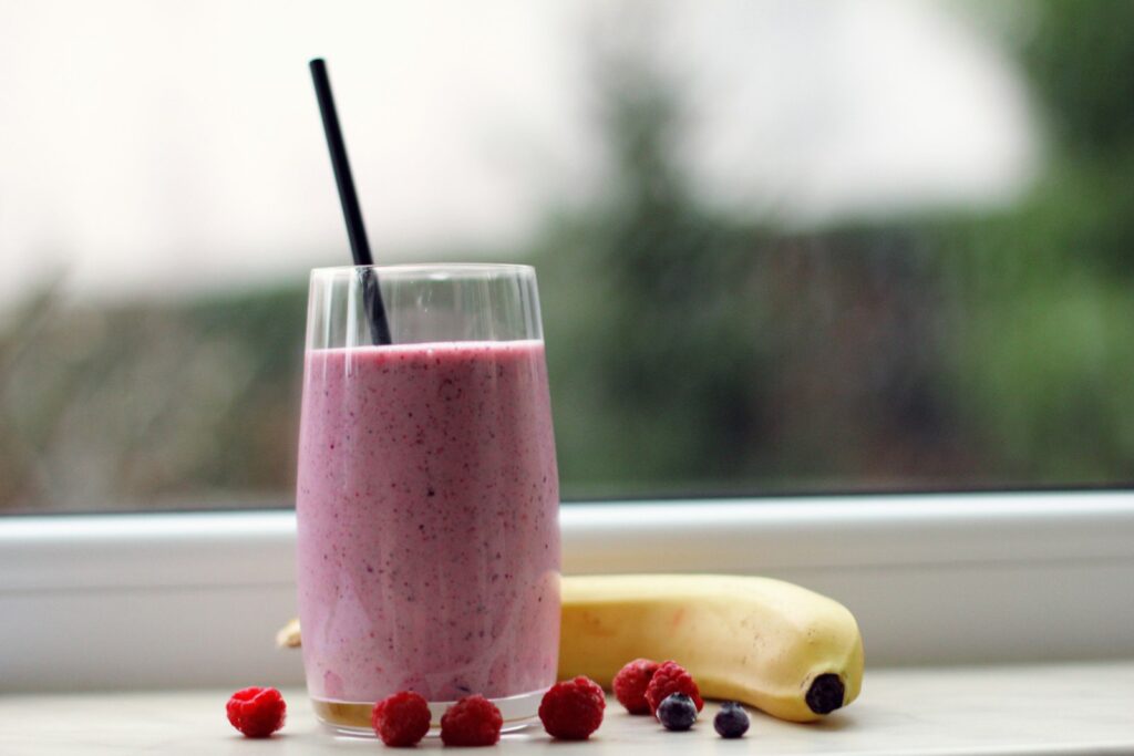 Pink smoothie in a glass beside berries and a banana