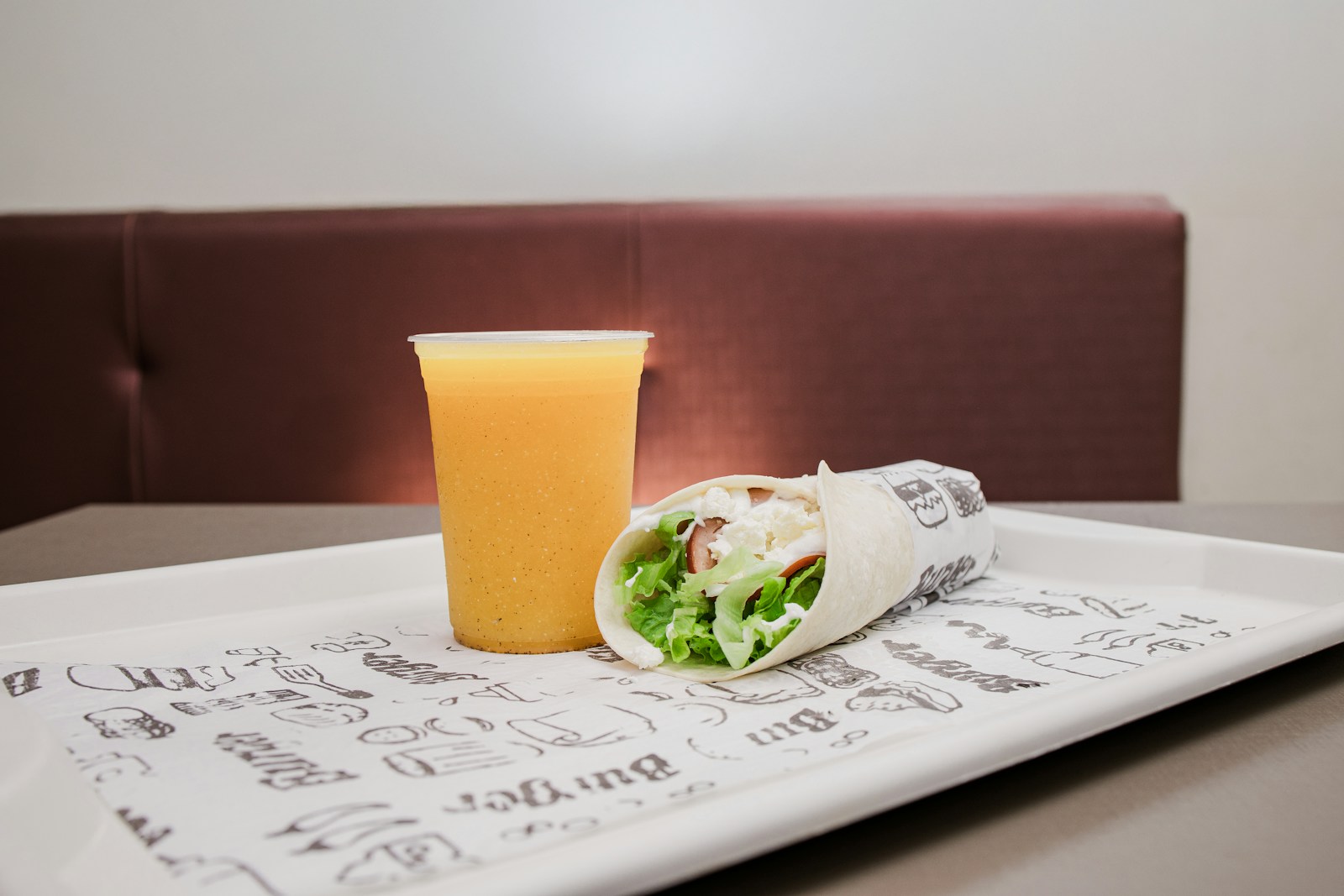 A takeaway wrap and a cup of orange drink on a tray