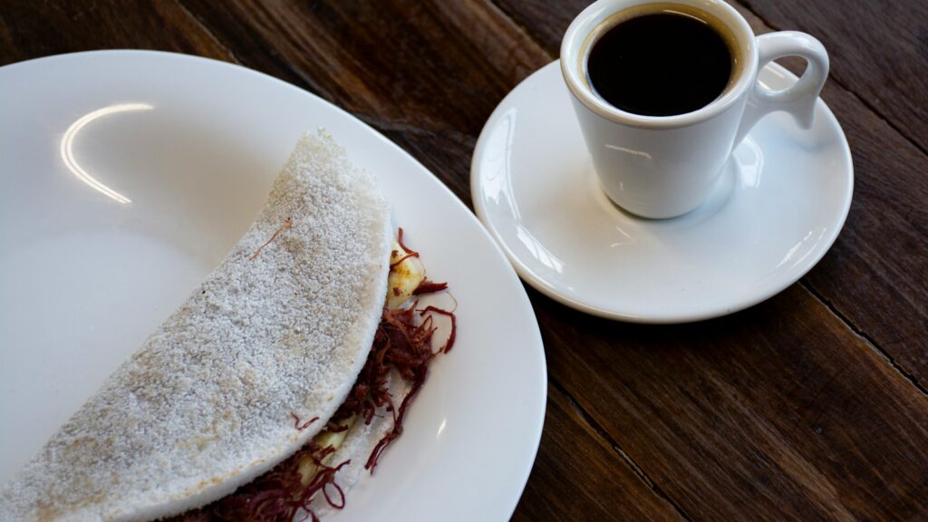 A folded tapioca flatbread served beside a cup of coffee