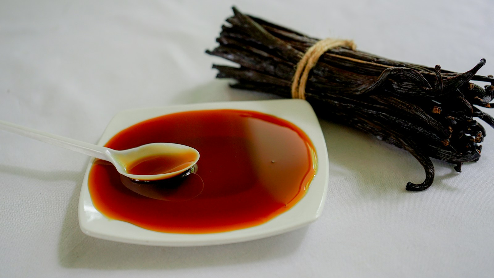 A dish of vanilla preparation beside a tied bundle of vanilla beans