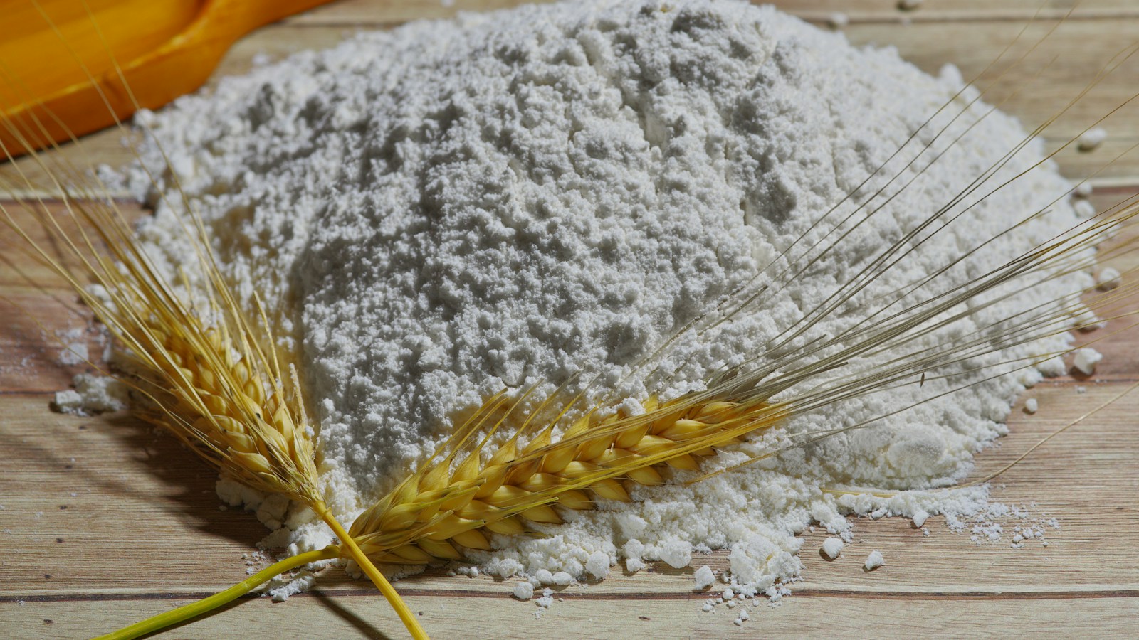 A mound of flour beside wheat heads on a wooden board