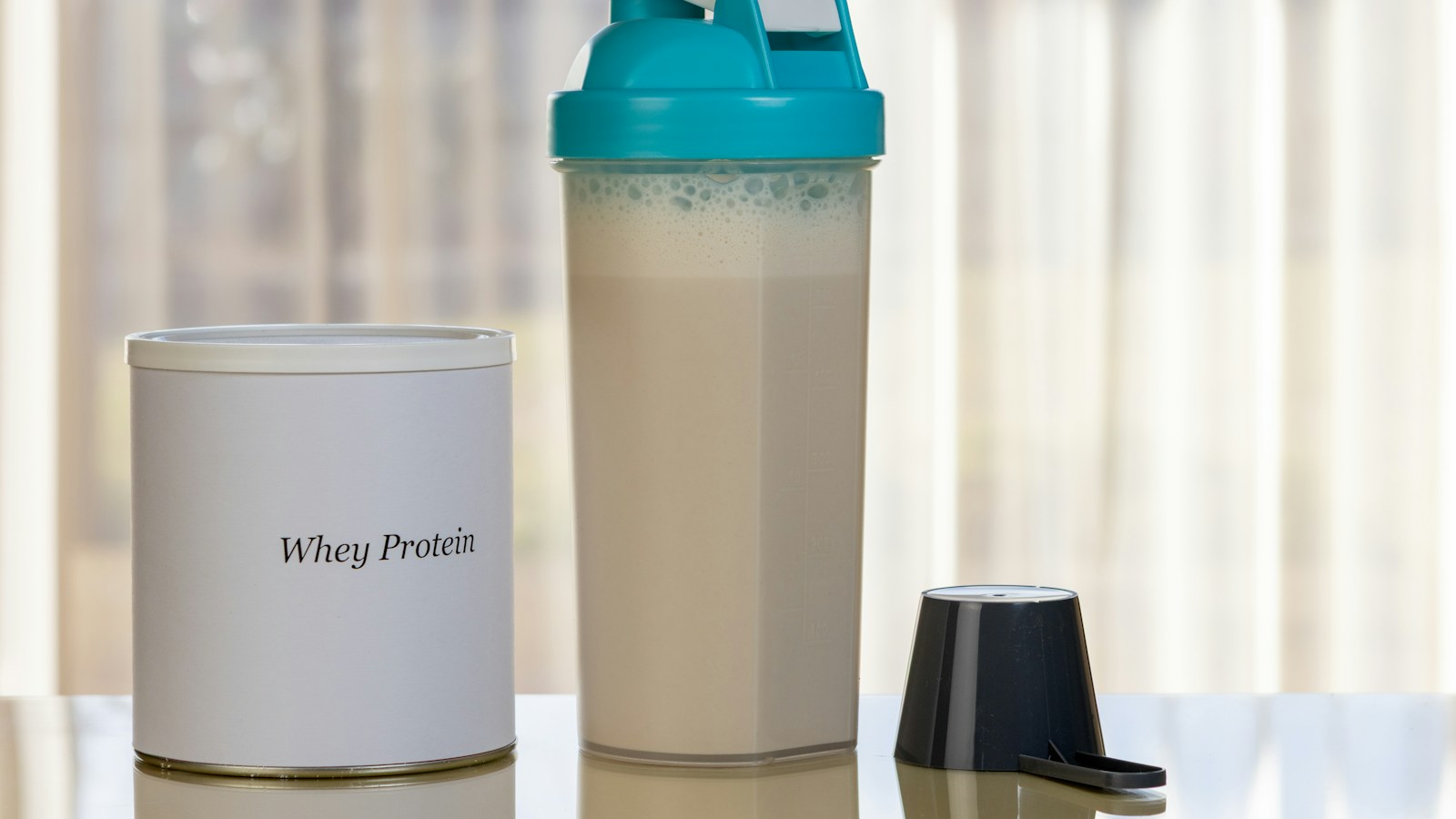 A whey protein container beside a shaker bottle