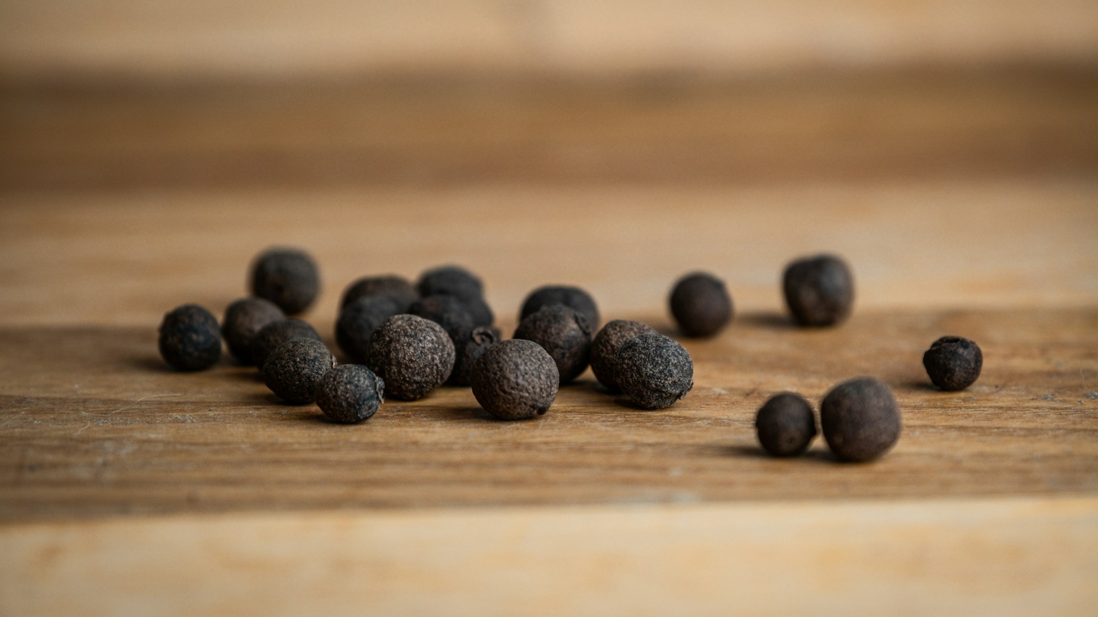 Whole allspice berries scattered on a wooden board