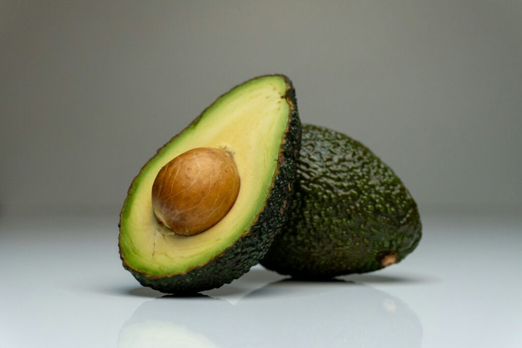 A whole avocado beside a cut half on a light background