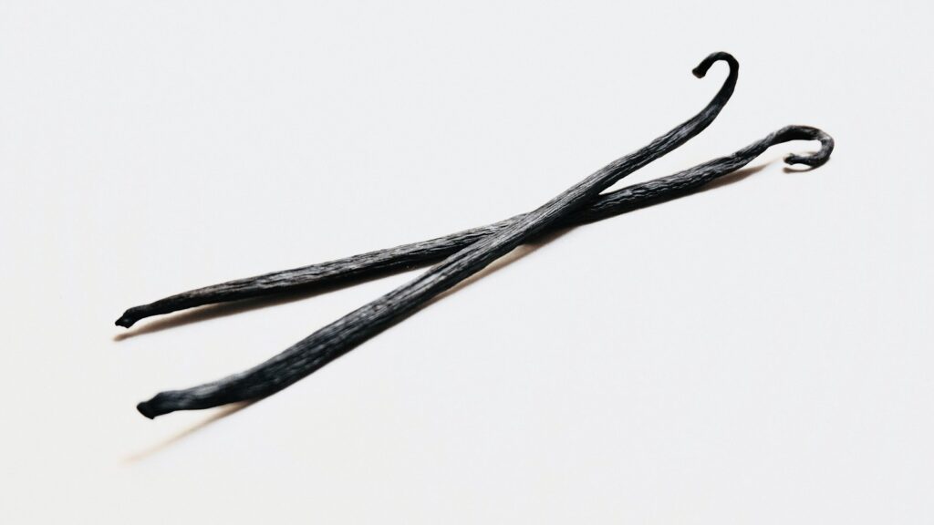Two dark vanilla beans on a light surface
